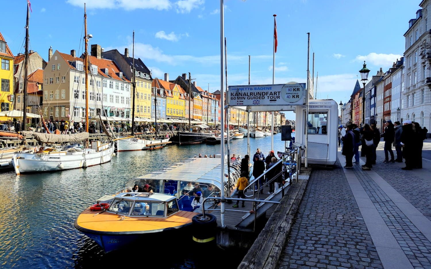 kopenhagen Nyhavn Canal harbor with yellow boat, moored sailboats, and colorful buildings along a sunny waterfront promenade. kopenhagen nyhavn