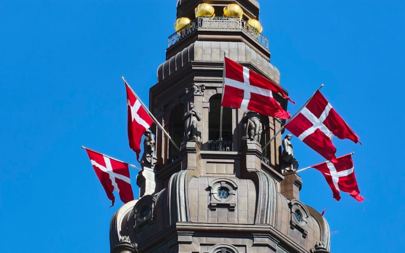 Kopenhagen Danish flags flying from a stone tower against a bright blue sky. Copenhagen Card