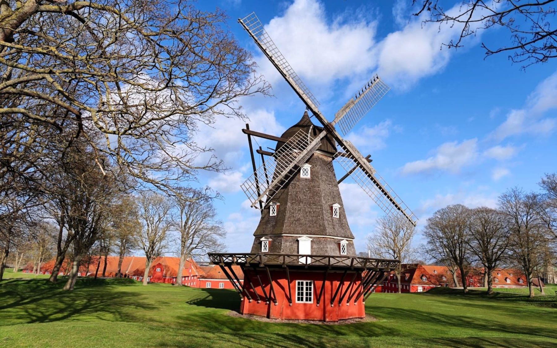 Kopenhagen Windmühle Historic windmill with black sails on a grassy field under a blue sky with clouds