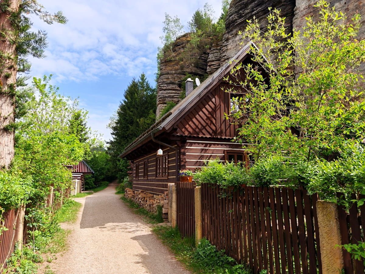 Bauernhaus in Kost - Böhmisches Paradies Narrow gravel path beside rustic wooden cottages and lush green trees under a bright blue sky.