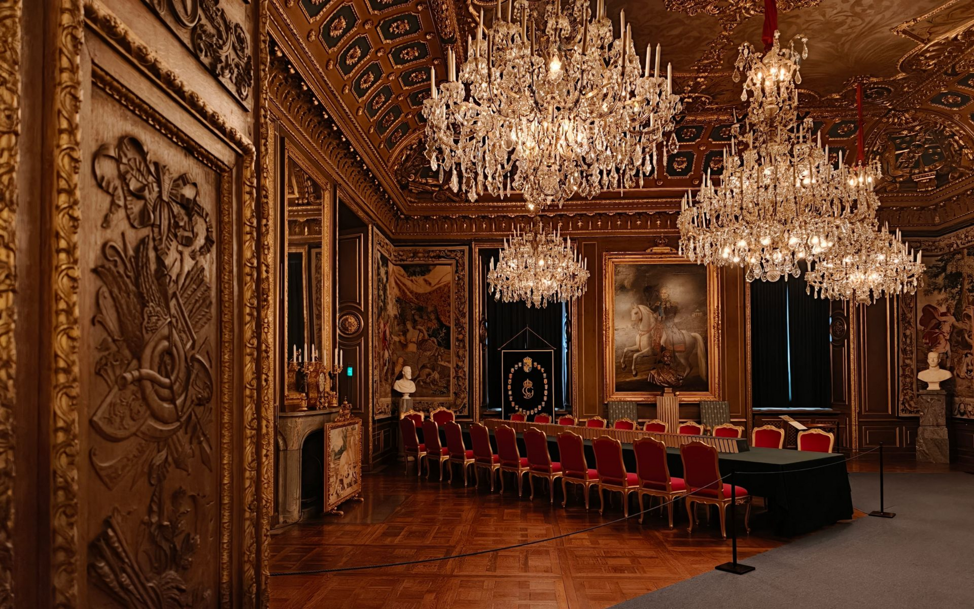 Stockholmer Schloss Ornate gold ballroom with crystal chandeliers and rows of red chairs around a long table