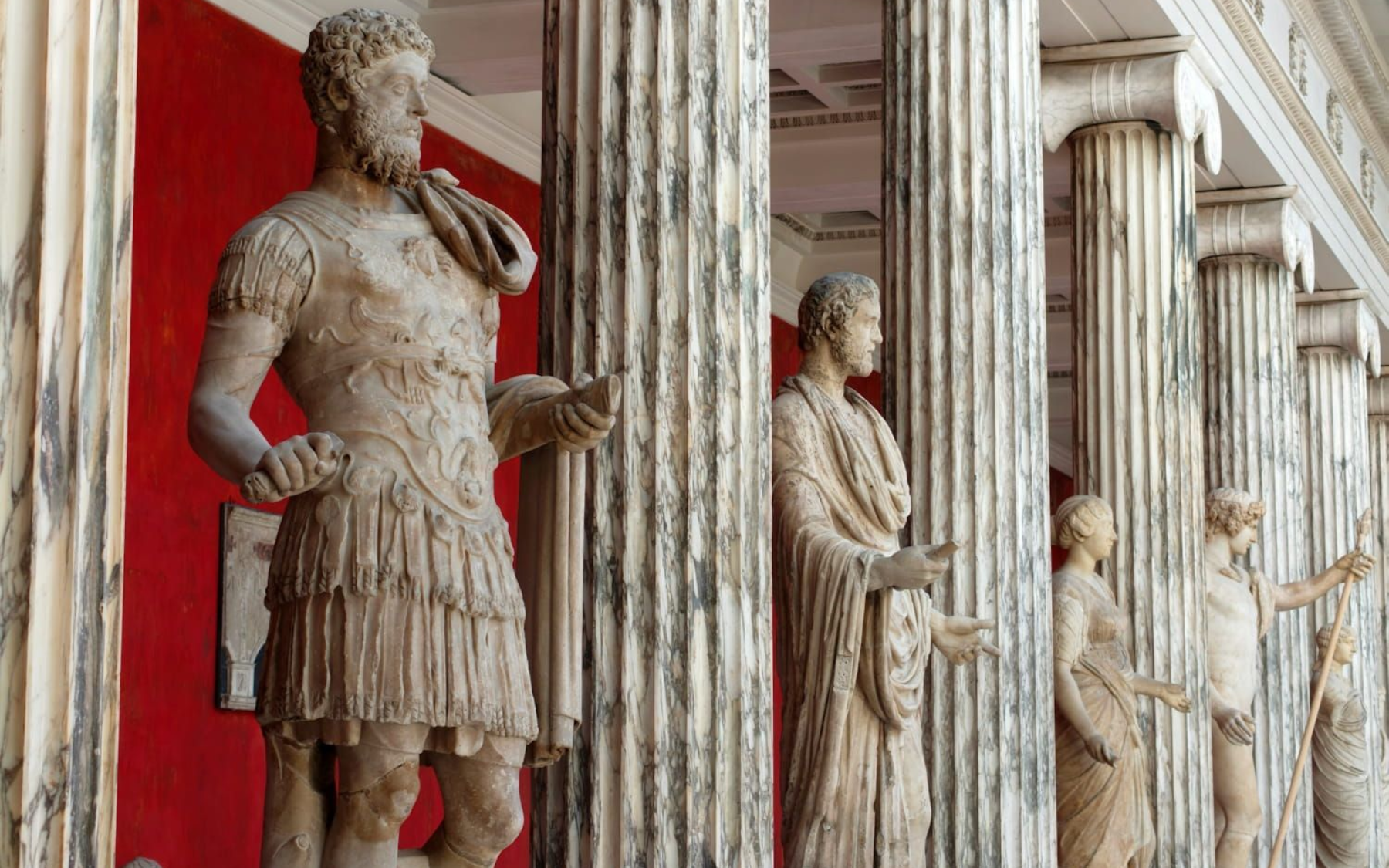 Ny Carlsberg Glyptotek Row of classical stone statues in a colonnaded museum hallway with a red wall backdrop.