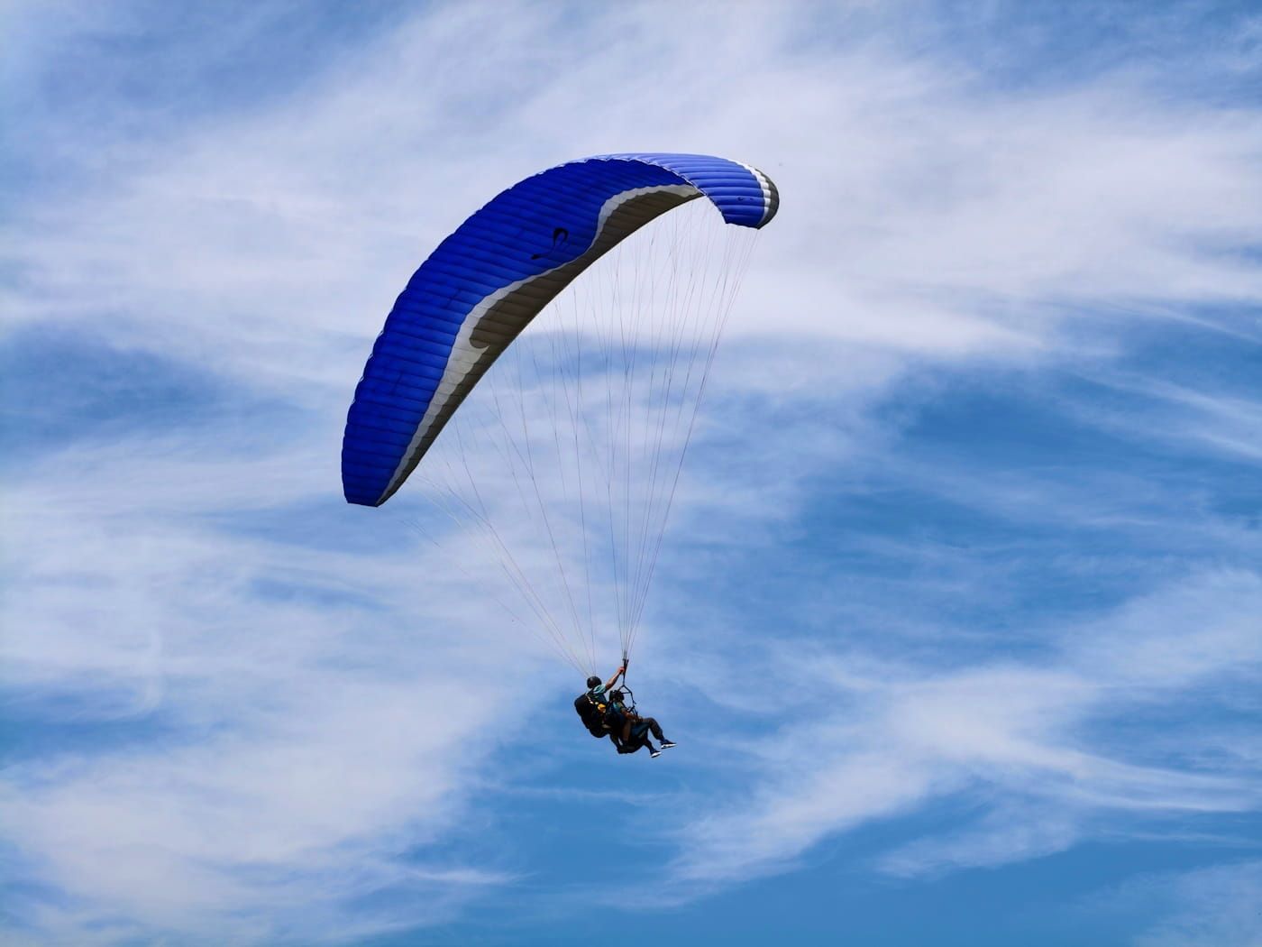 Paraglider with a blue canopy glides against a cloudy sky