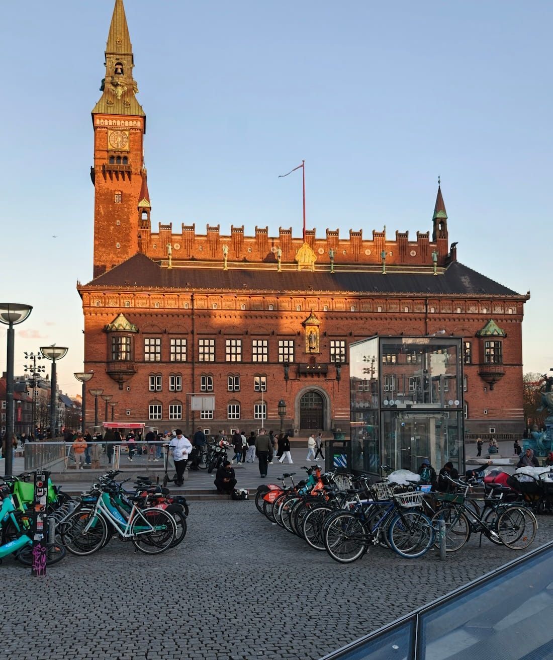 Historic red-brick city hall at sunset, with bicycles and people in the foreground.