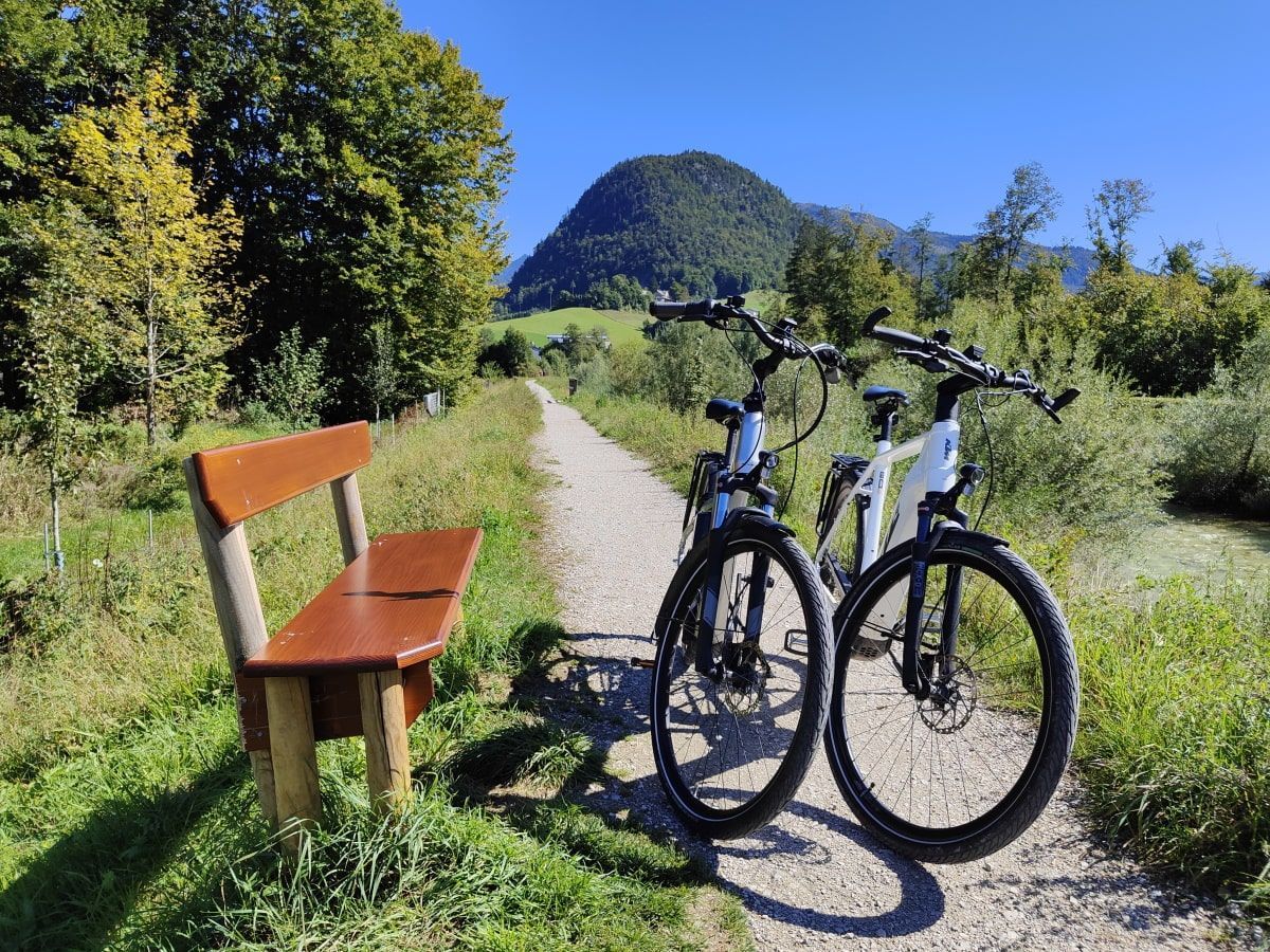 Radtour Salzkammergut Two bikes parked on a path next to a bench, mountain in the background. Sunny day.