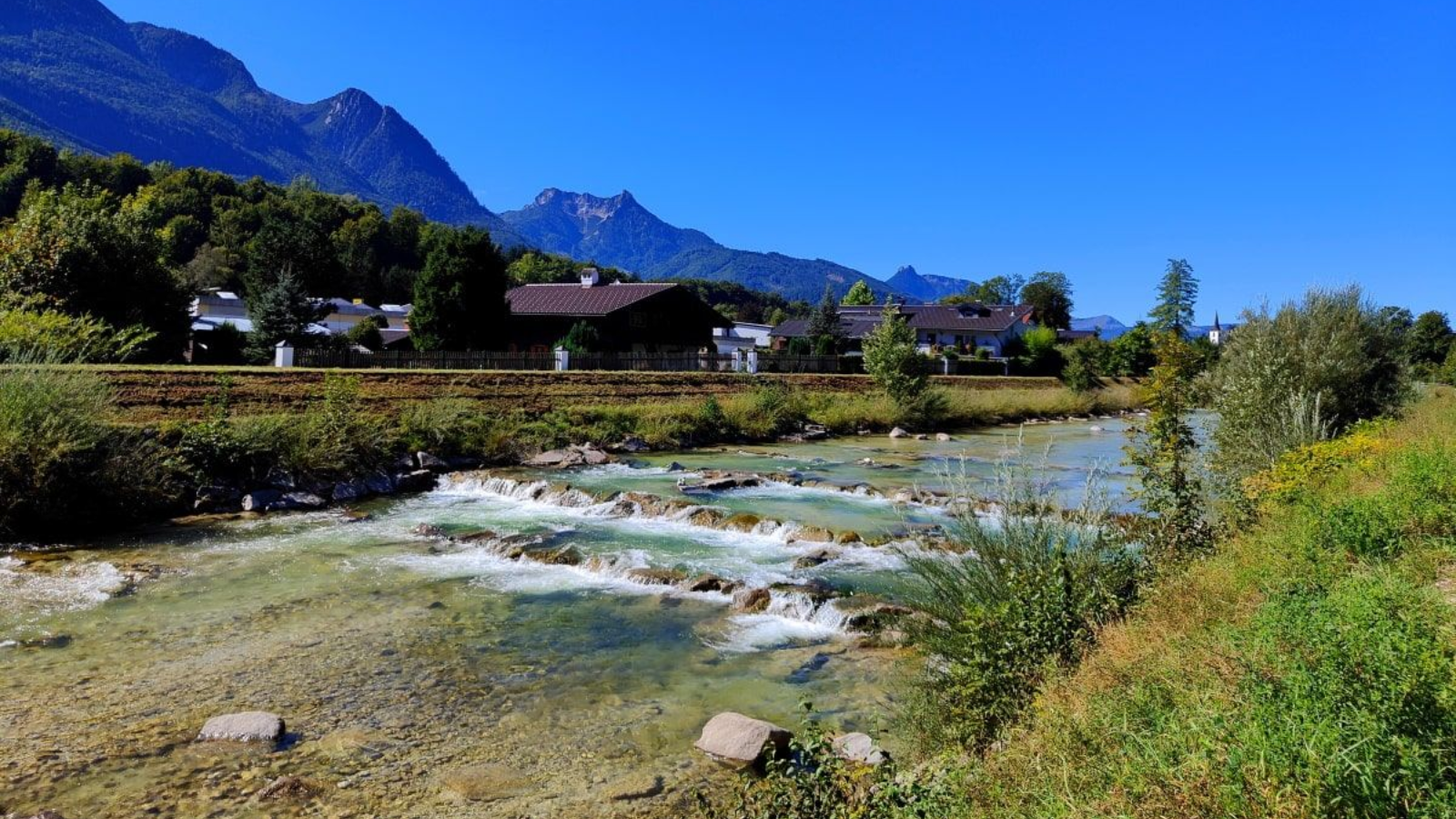 Ischl A river flows past a village and mountains under a clear blue sky.