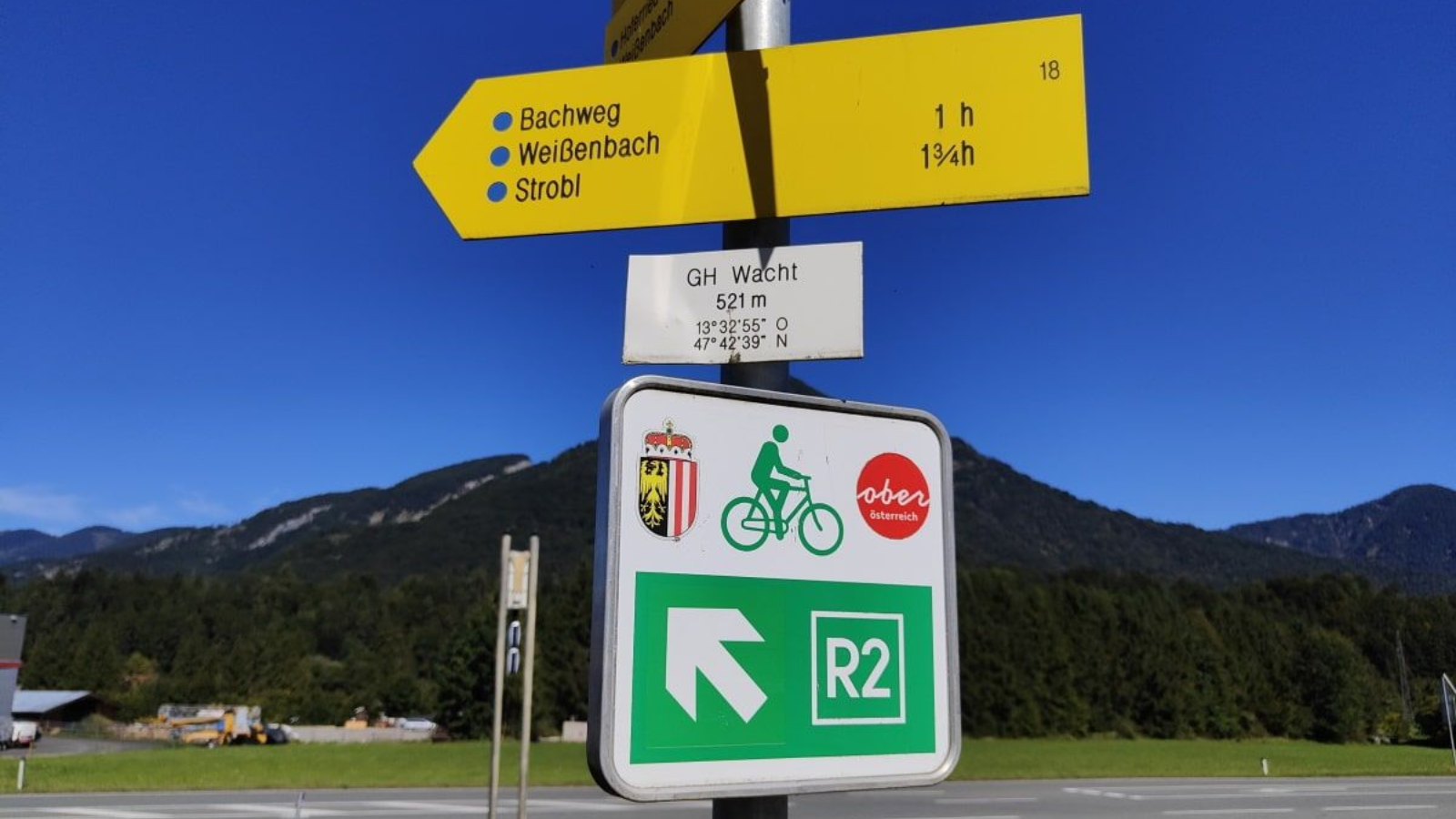 R2 Salzkammergut Yellow directional sign and bike route marker, with mountain backdrop under blue sky.
