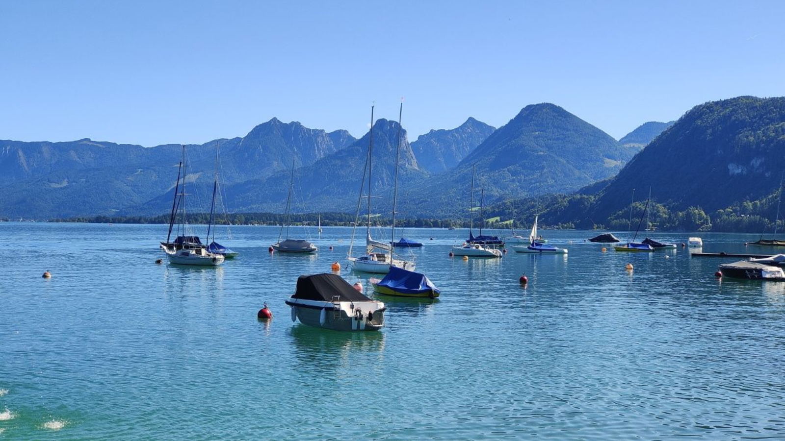 Salzkammergut St.Gilgen Boats bob on turquoise water in a lake, backed by green mountains under a clear blue sky.