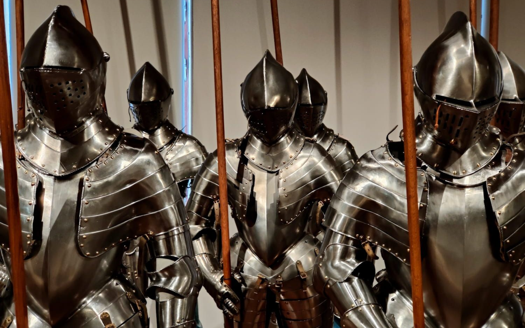 Schloss Ambras Innsbruck Row of shiny, medieval suits of armor, with helmets and spears, displayed indoors.