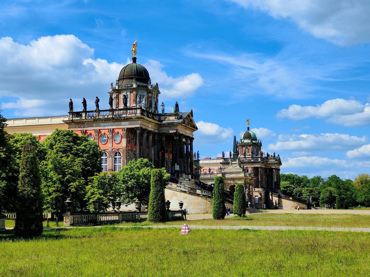 Ornate palace with a large dome under a blue sky with white clouds, in a grassy area.