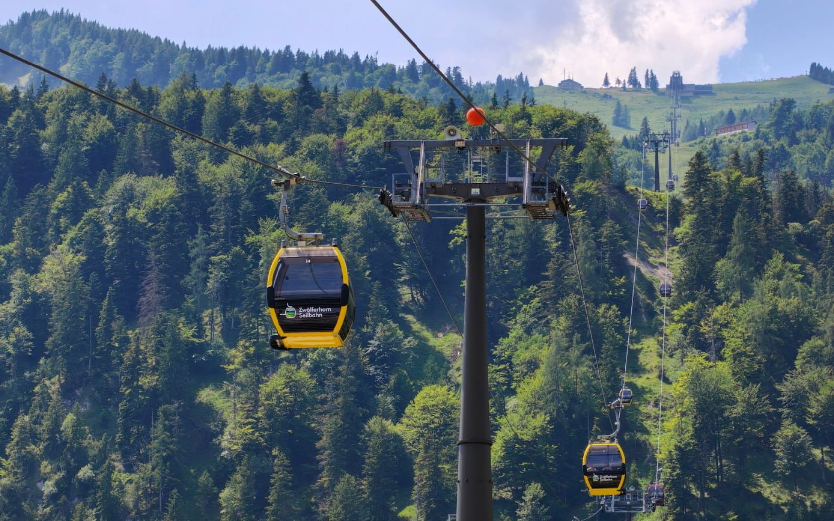 Zwölferhorn Seilbahn Yellow gondola cars on a cable line over a forested mountain valley