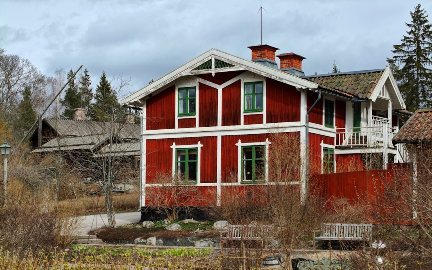 Skansen Stockholm Skansen Stockholm. Red wooden house with white trim and a chimney, seen beside a paved path and bare trees.