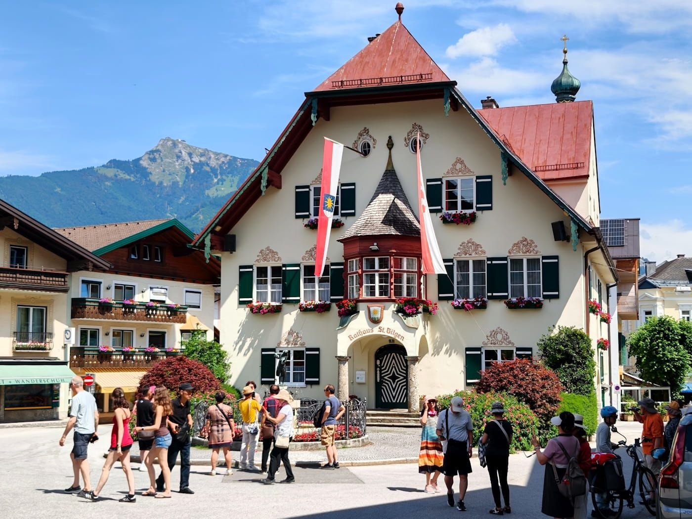 St. Gilgen Town square flags, and people walking in front of mountains.