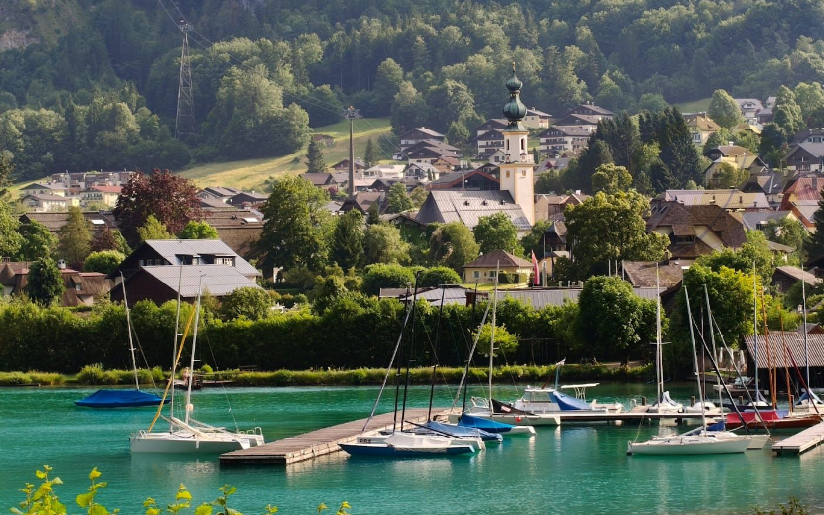 St. Gilgen Marina with sailboats on turquoise water, backed by a village and church in a green hillside valley