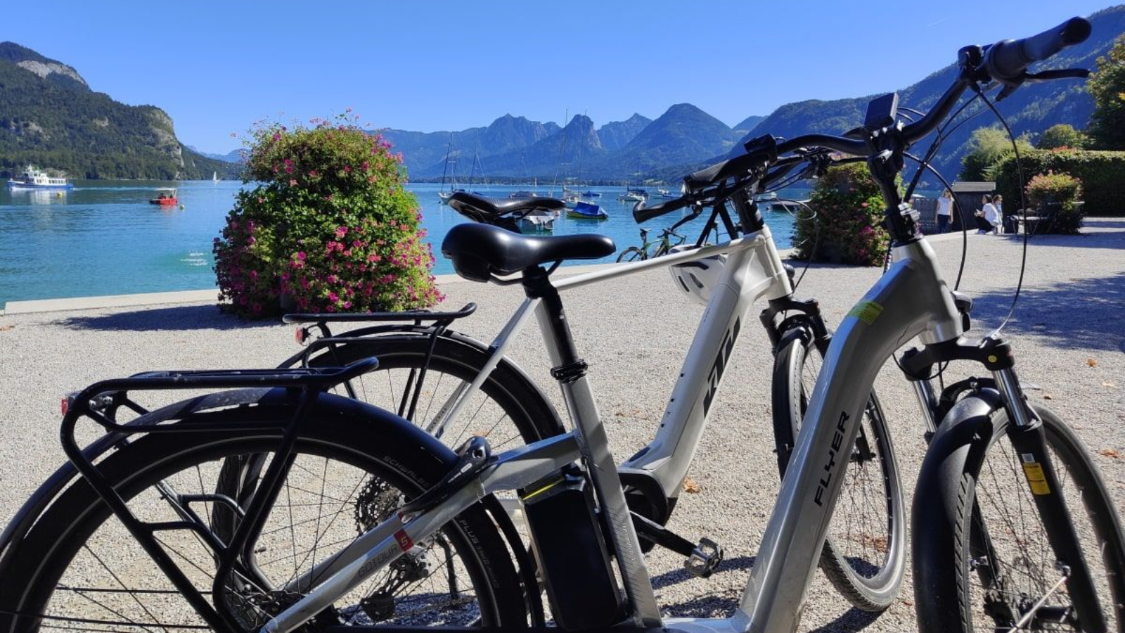 St.Gilgen Two electric bikes parked by a lake with mountains in the background under a clear blue sky.