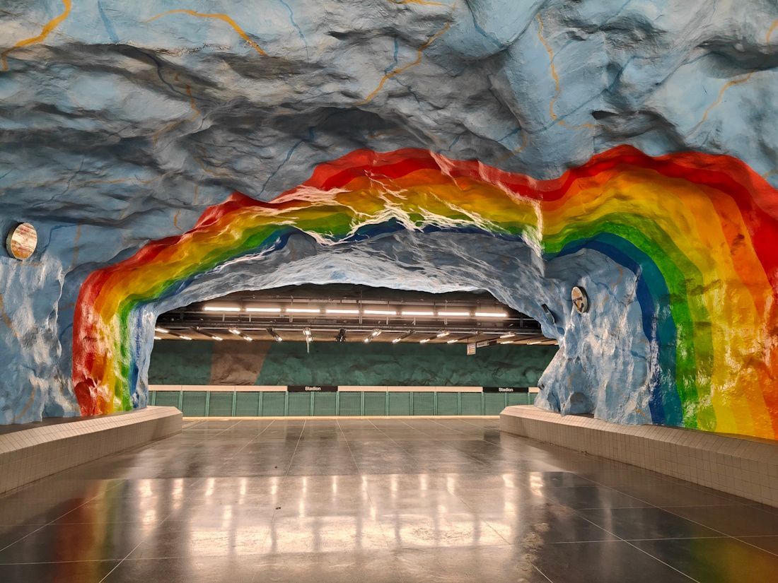 Underground stadium tunnel with a rainbow-painted rock arch and a glossy floor leading to seats beyond
