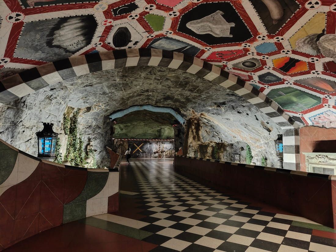 Arched tunnel with mosaic ceiling, checkered floor, and a lit lantern on the left wall.