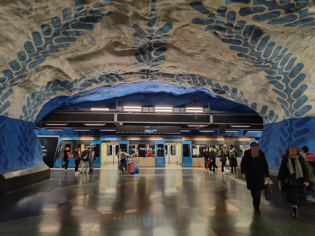 Subway station entrance framed by blue mosaic arch, with commuters walking on a wet floor