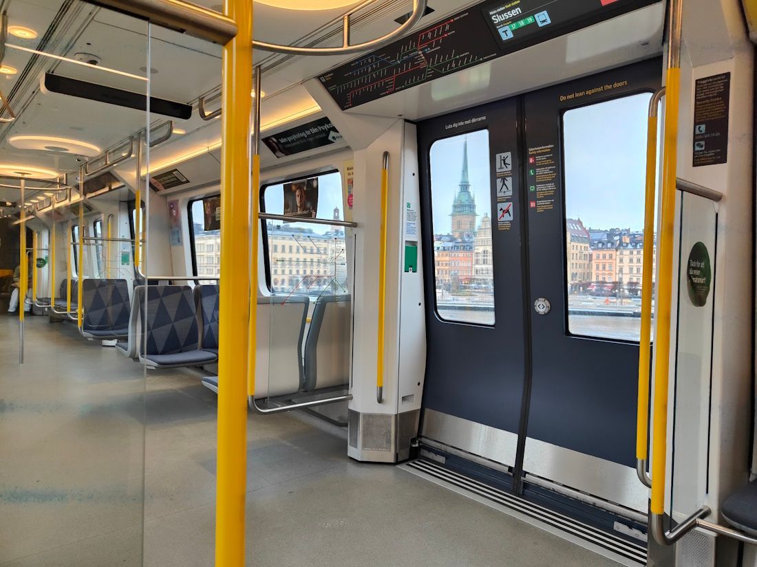Empty modern train interior with yellow poles, blue seats, and city views through the windows