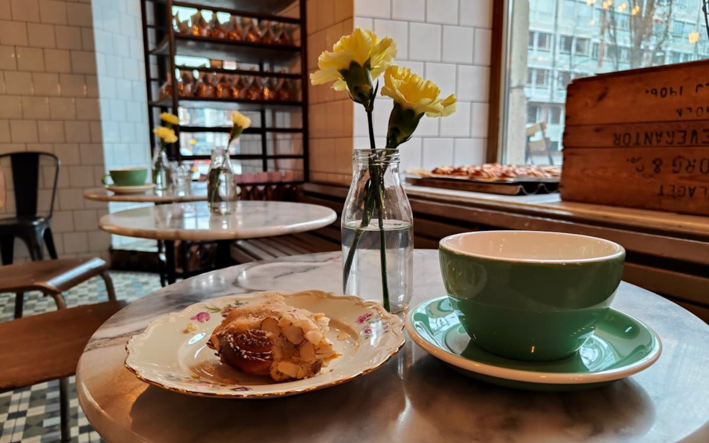 Fika Stockholm Stockholm Fika. Cafe table with pastry, green cup and yellow flowers by a window