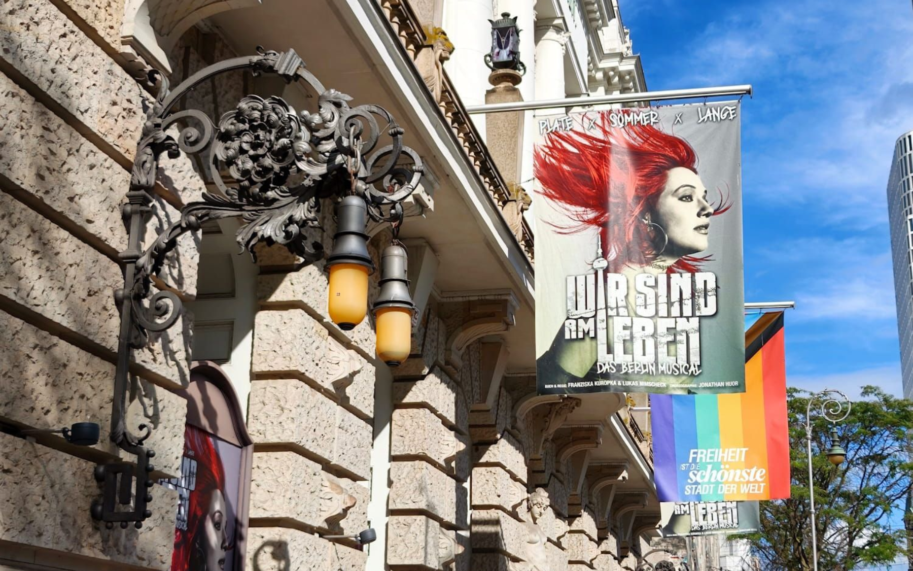 Theater des Westens Berlin Street with ornate building facade and colorful hanging banners under a blue sky.