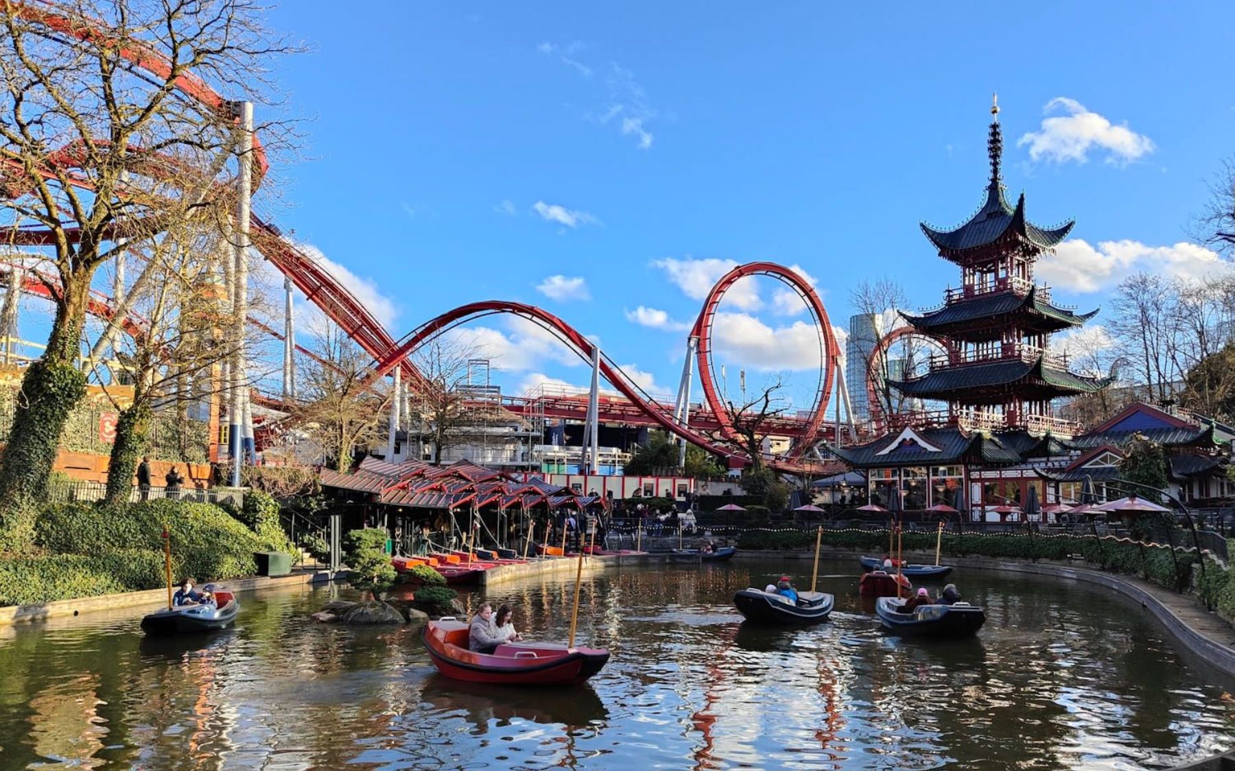 Tivoli Amusement park lake with red roller coaster loops and a pagoda-like tower under a blue sky