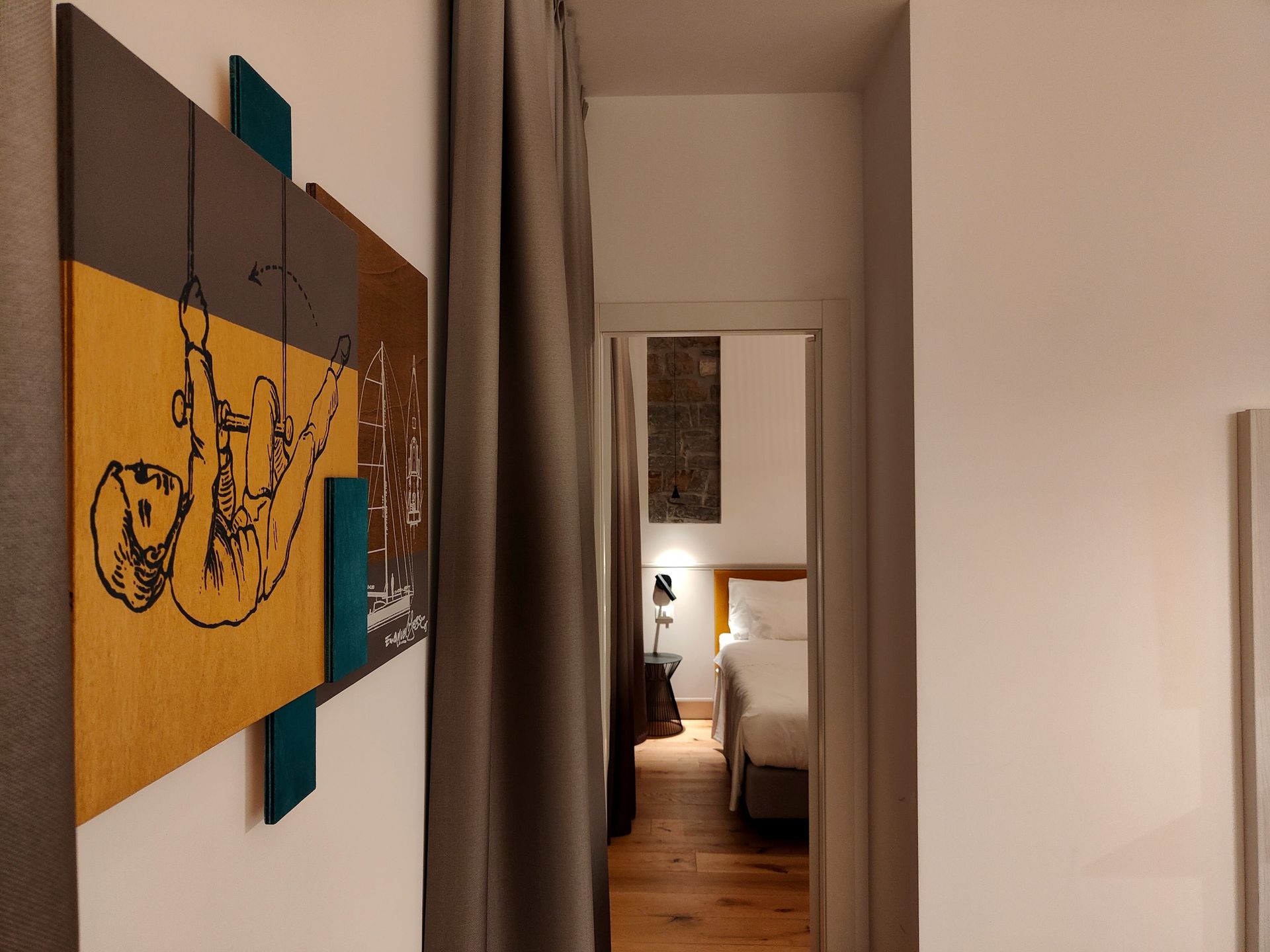 Urbanauts Studios Ginnastica Triest Narrow hallway with a yellow wall hanging on the left and a doorway revealing a lit bedroom ahead.
