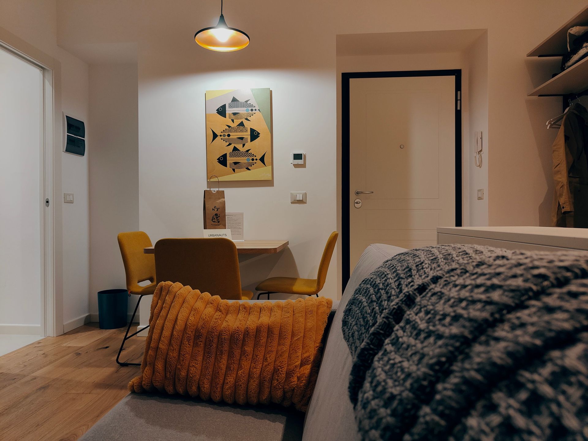 Urbanauts Studios Ginnastica Triest Cozy bedroom with a bed, mustard chair, wall art, and warm lighting in a minimalist apartment