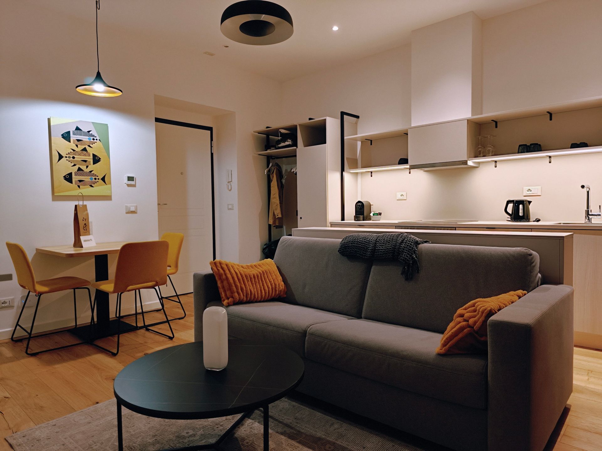 Modern apartment living room and kitchen with gray sofa, dining table, and warm lighting