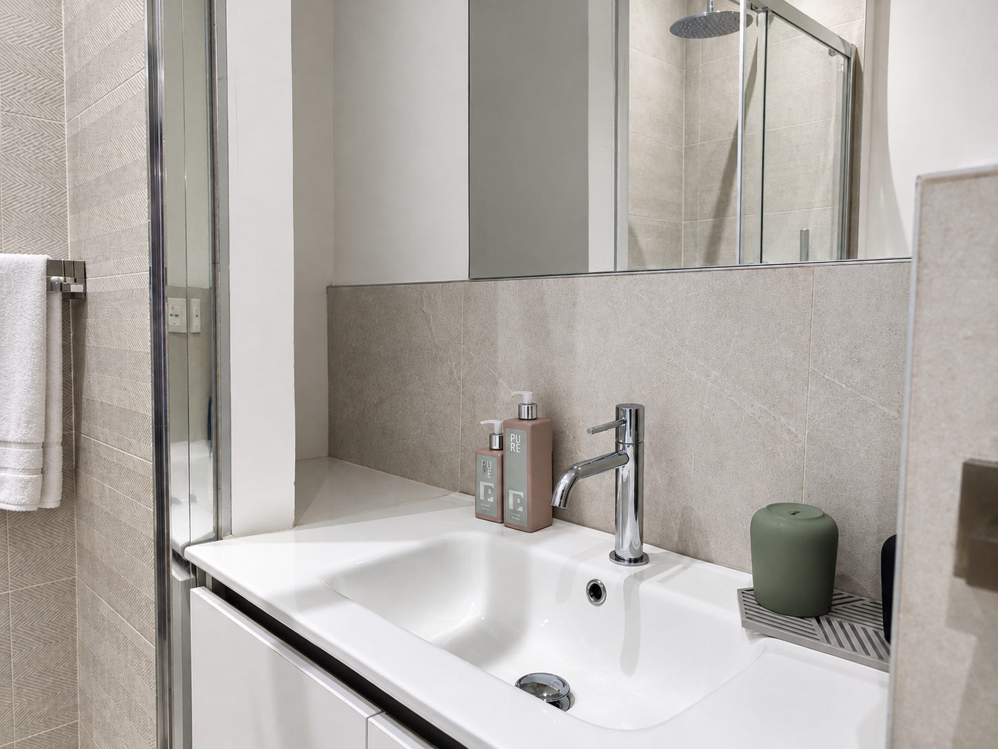 Small bathroom sink with chrome faucet, mirror, soap dispenser, and green container on the counter.