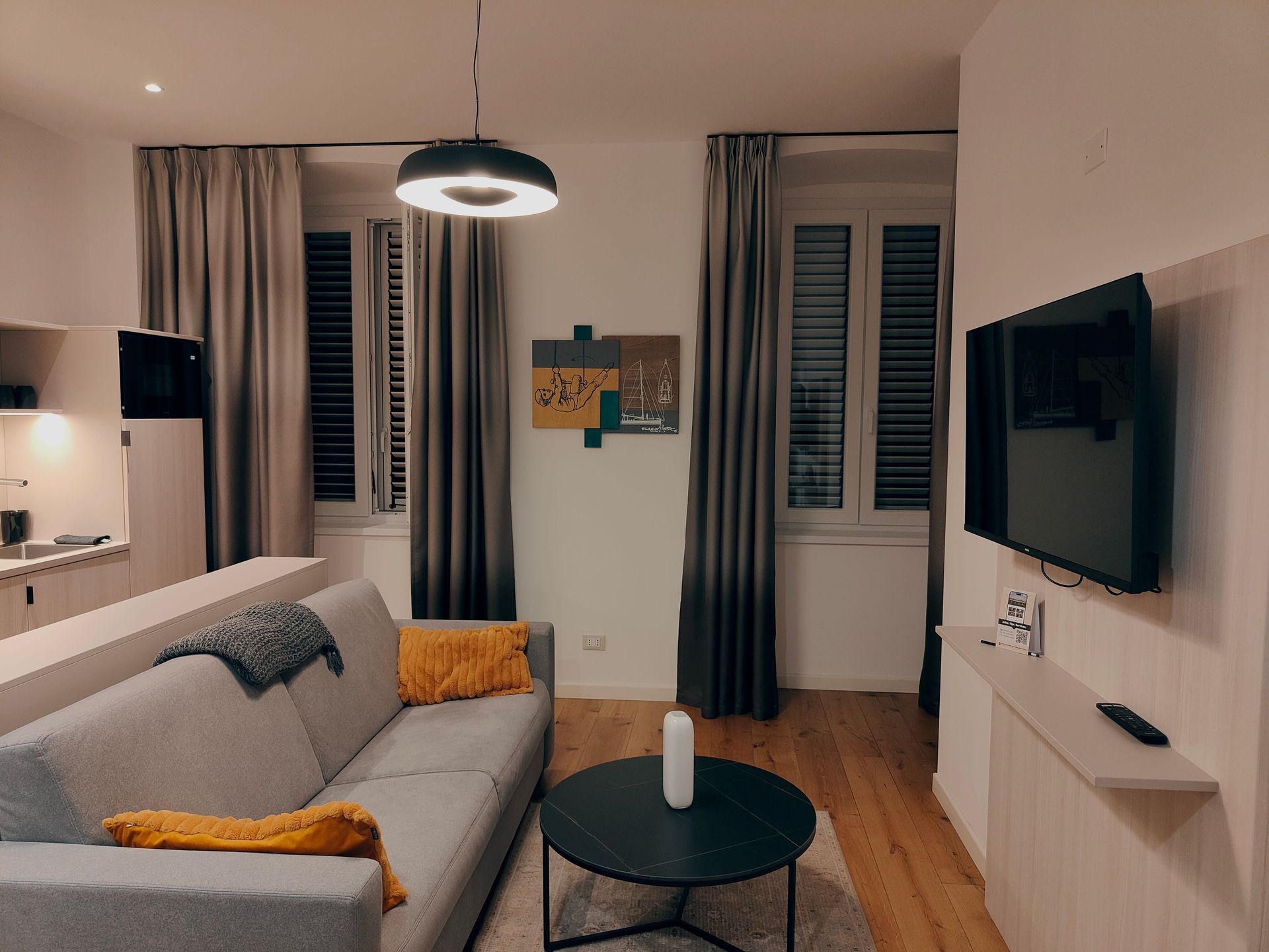 Modern living room with gray sofa, black coffee table, wall-mounted TV, and curtained windows