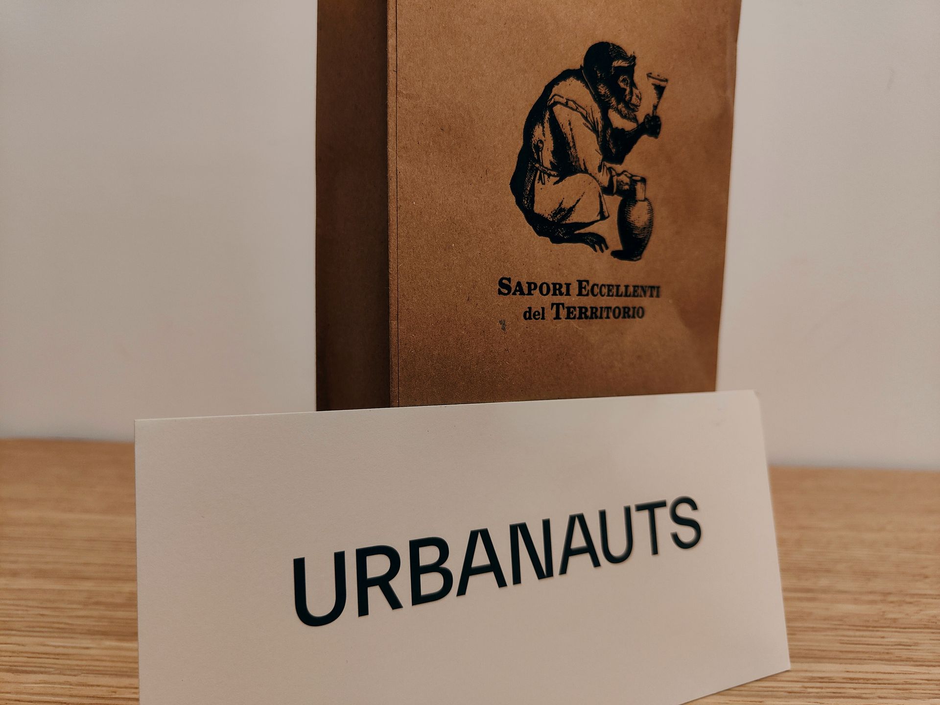 Urbanauts White card reading “URBANAUTS” in front of a brown paper bag with a black figure logo.