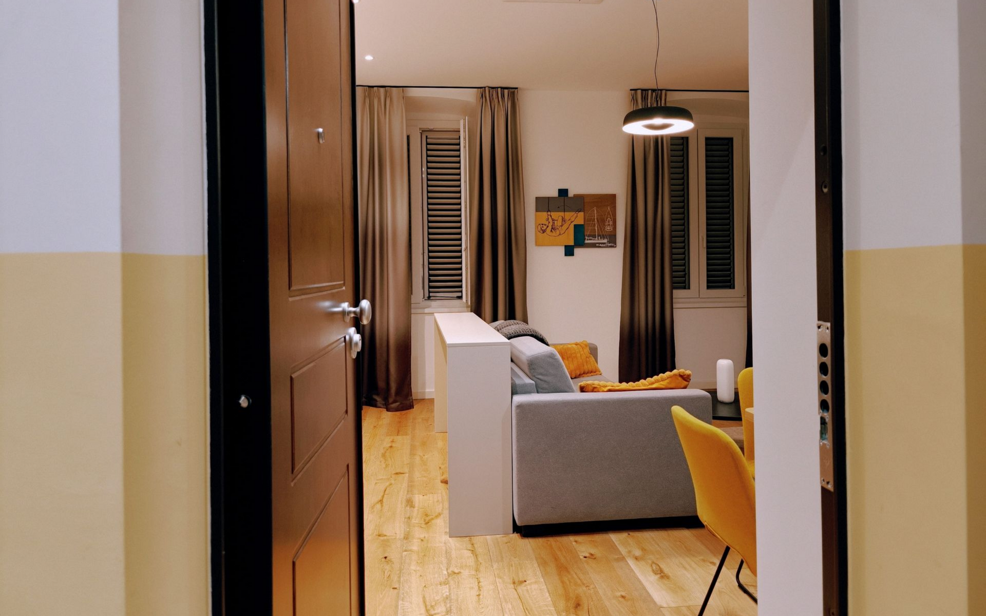 Urbanauts Studios Ginnastica Triest Living room with gray sofa, yellow chair, and pendant lights in a narrow hallway-style apartment