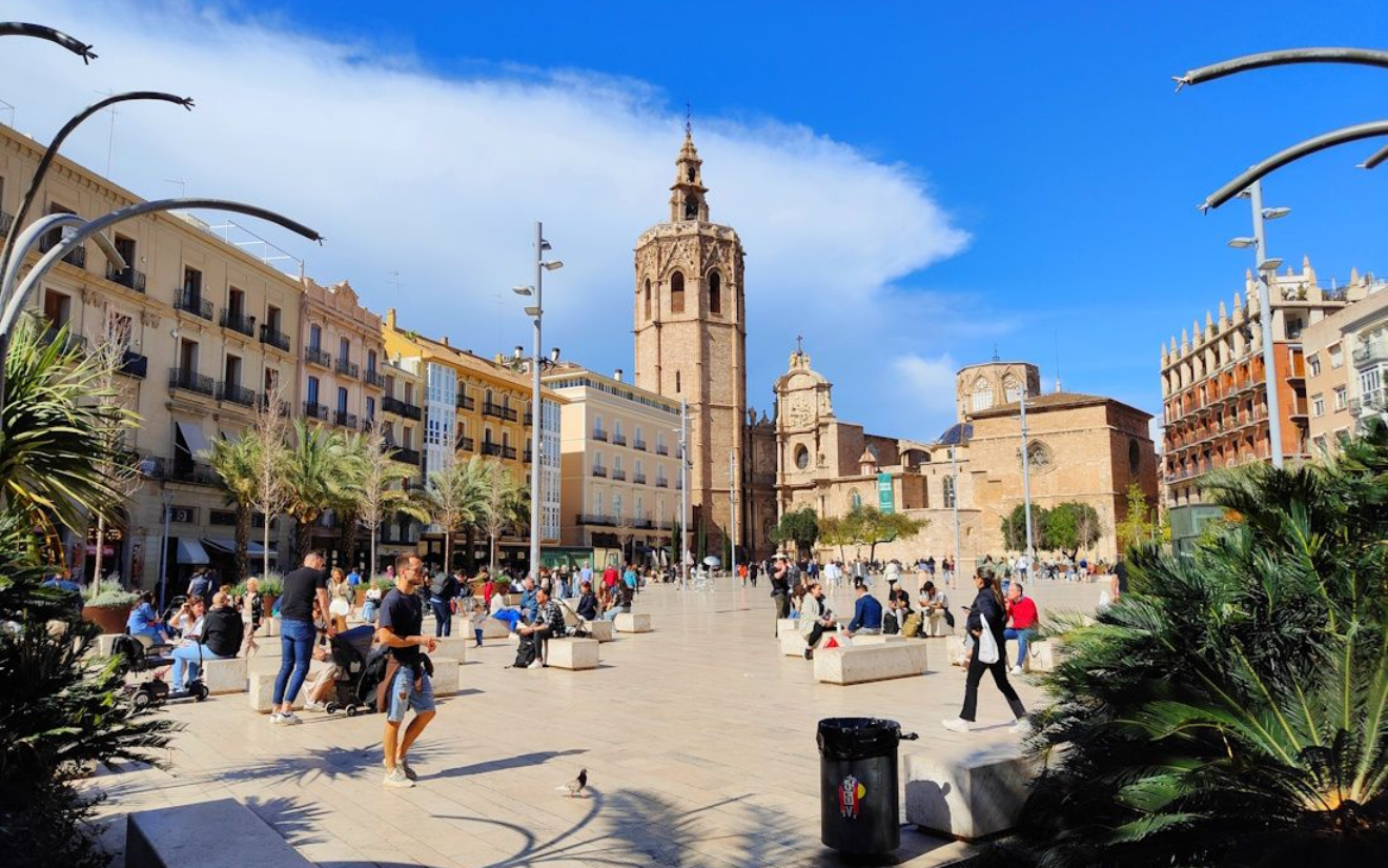 Valencia People in a sunny plaza with a cathedral and buildings in Valencia, Spain.