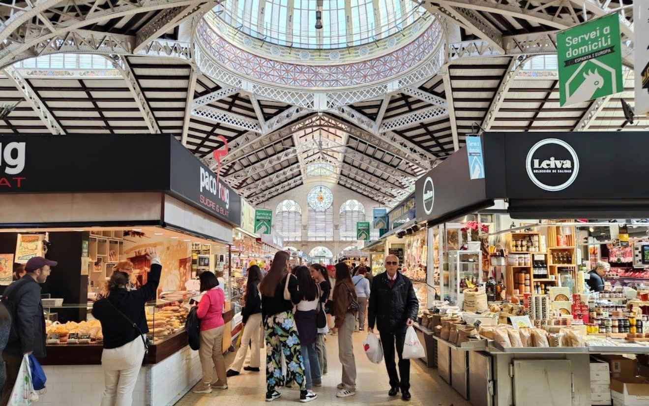 Mercado Central Exterior view of Valencia Central Market, a building with ornate, colorful tilework and arched entrances. People are entering.