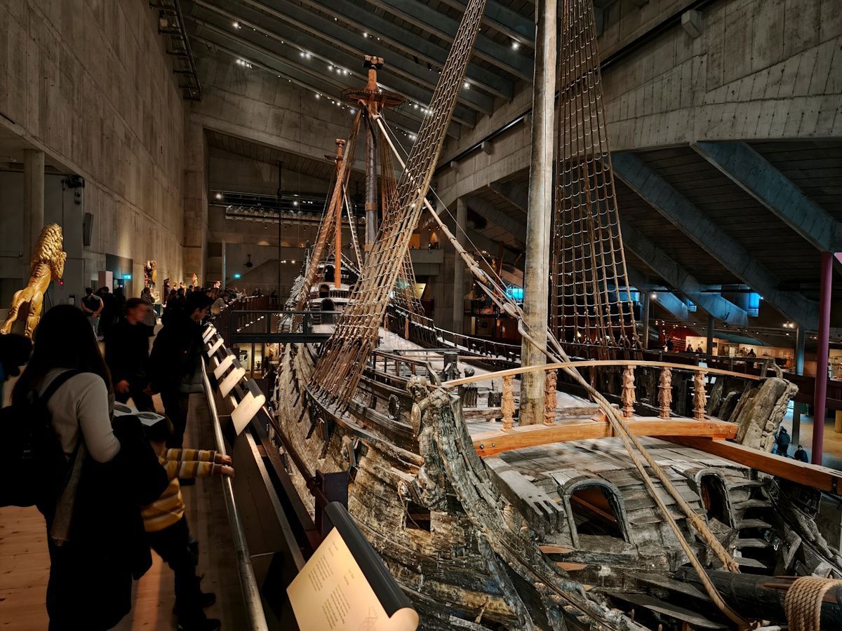 Vasa Museum Vasa Museum. Visitors view an excavated Viking ship in a large indoor museum hall, lit by warm lights.