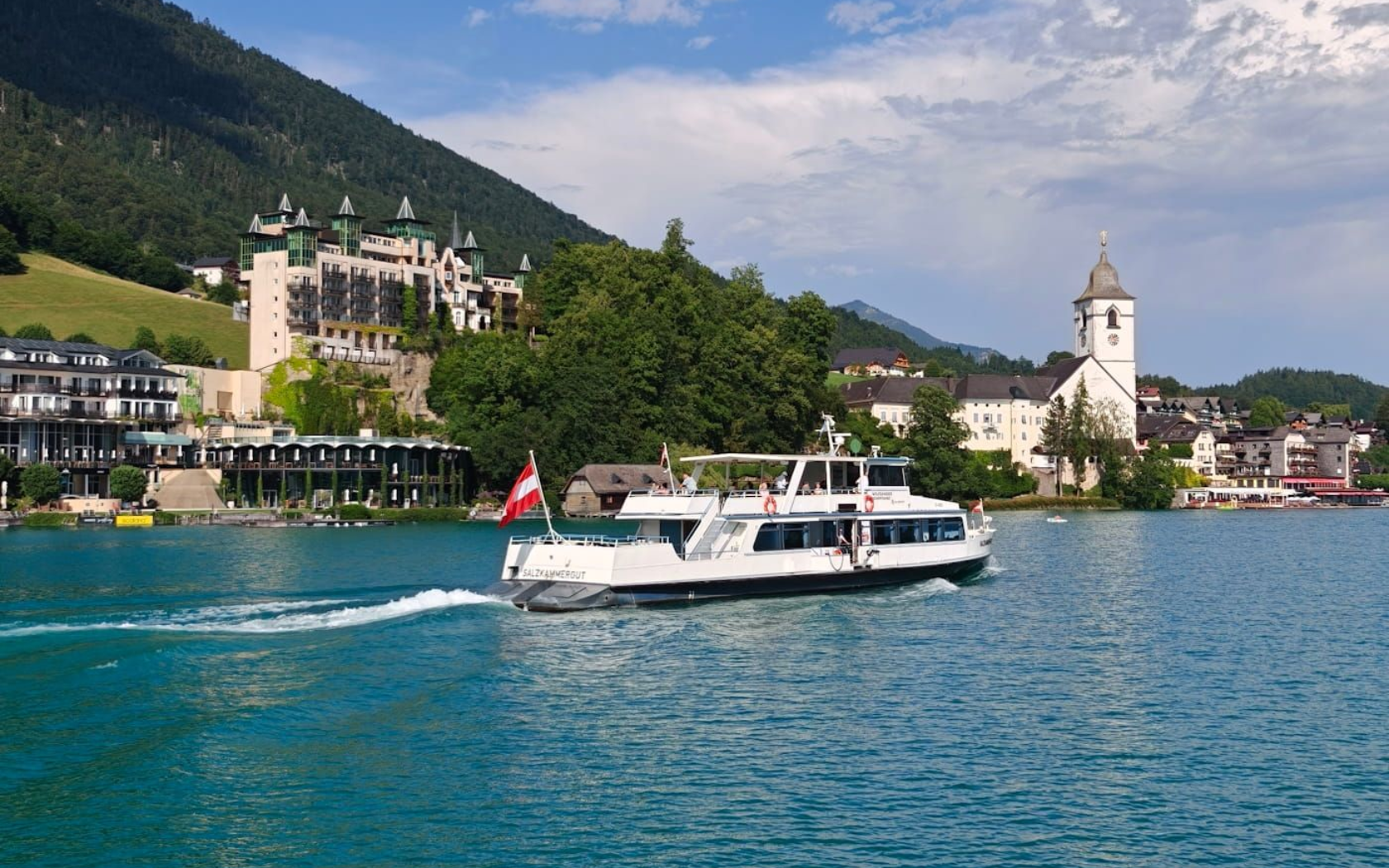 Wolfgangsee Schifffahrt White ferry cruising on a blue lake near a mountain town and church under a clear sky