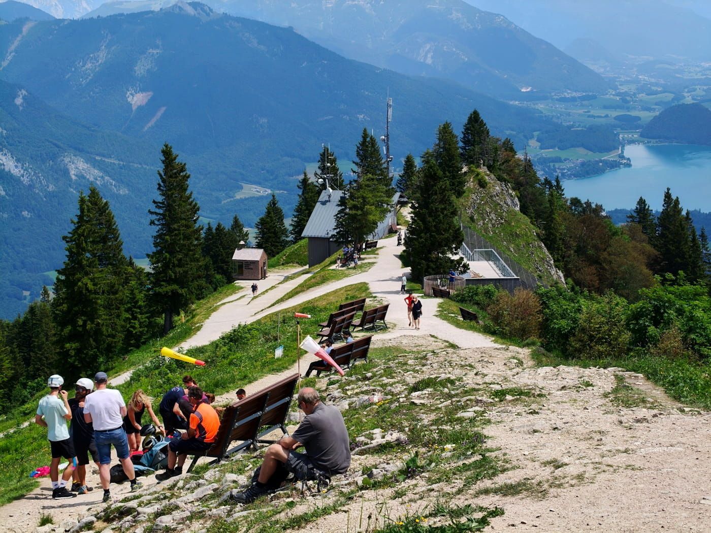Hikers resting on a mountain trail overlooking a blue lake and forested peaks