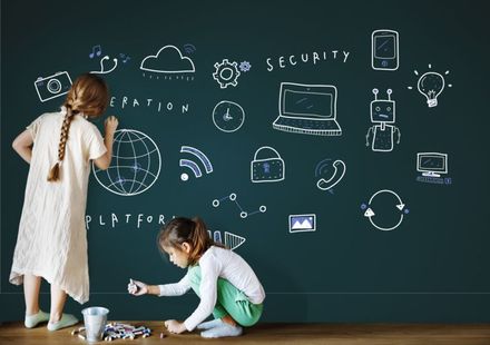 Two little girls are drawing on a blackboard with chalk.