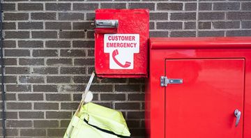 A red customer emergency box is attached to a brick wall.
