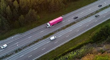 An aerial view of a pink semi truck driving down a highway.