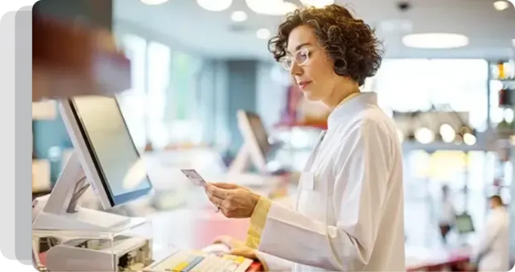 A female pharmacist is standing in front of a computer in a pharmacy.