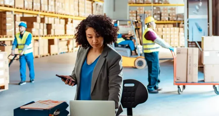 A woman is standing in front of a laptop computer in a warehouse.