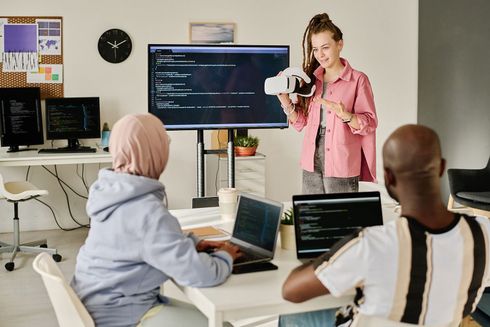 A woman is holding a virtual reality headset in front of a group of people.