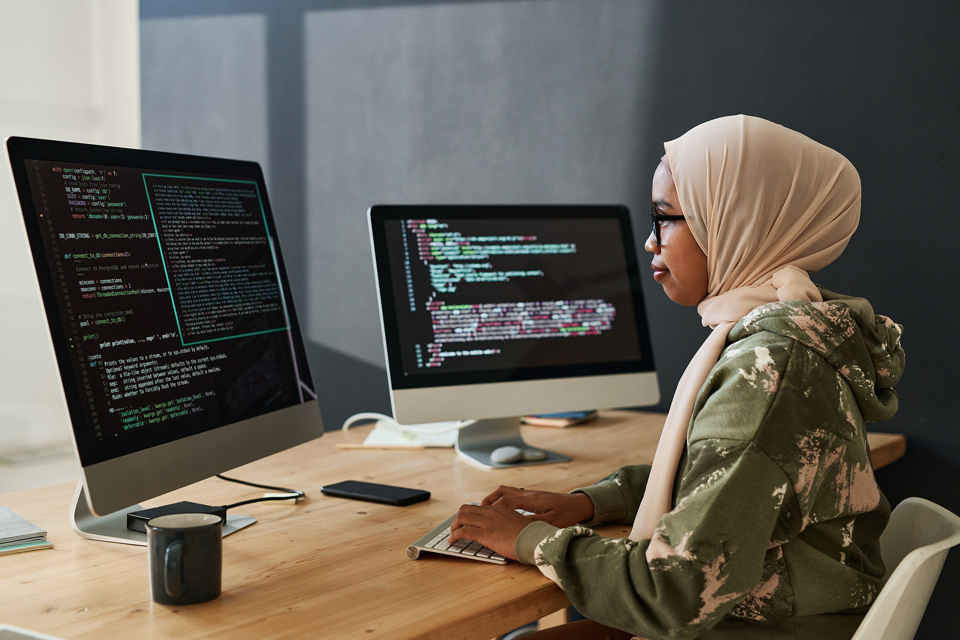 A woman in a hijab is sitting at a desk working on a computer.