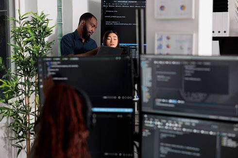 A man and a woman are sitting in front of computer monitors.