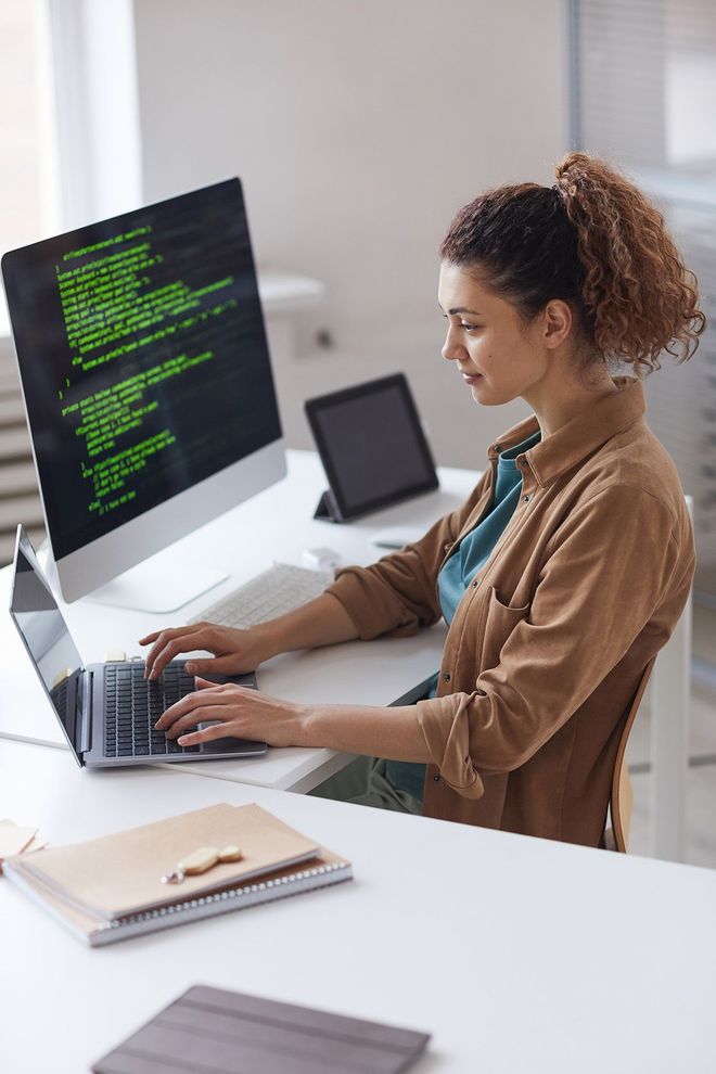A woman is sitting at a desk typing on a laptop computer.