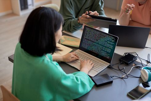 A woman is sitting at a table typing on a laptop computer.