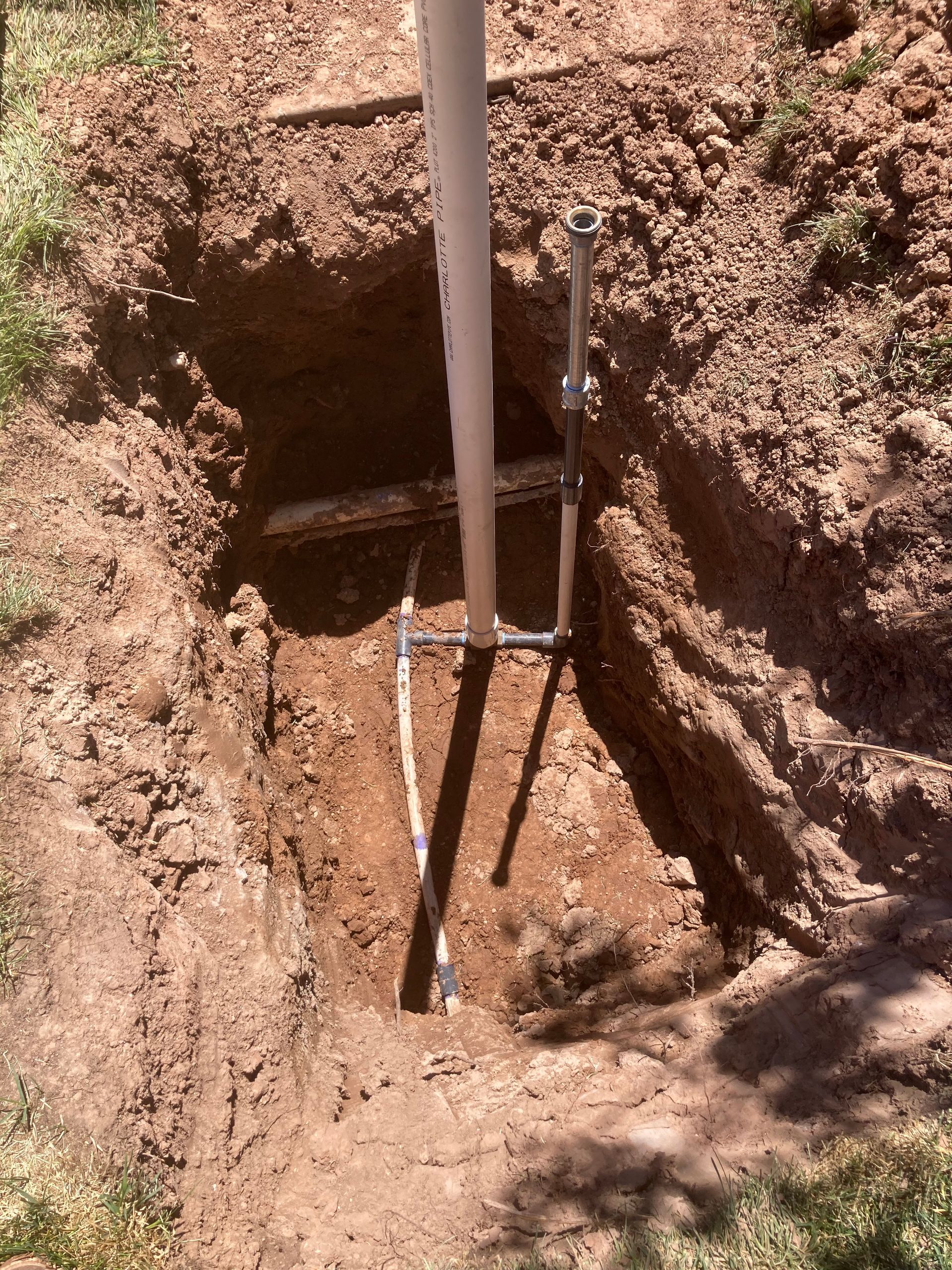 A hole in the ground with a white pipe and metal supports installed, in a yard.