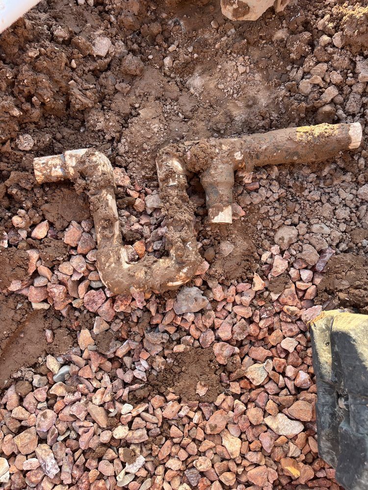 Brown PVC pipe, dug up from soil and small red gravel, is in a Z shape.